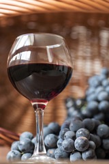 A glass of fragrant red wine and bunches of blue grapes
