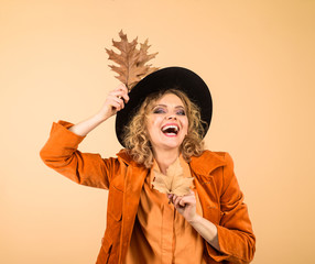 Woman autumn fashion. Autumn girl in black hat. Happy woman with autumn leaves in orange jacket. Fashionable woman with autumn leaves in hand. Fall. October. Beautiful model girl with autumnal leaves.