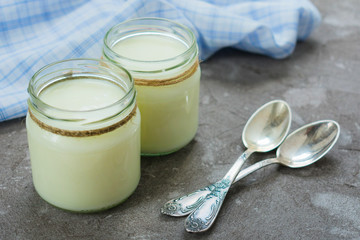 Greek yogurt in glass jars with spoons on a gray textural background.