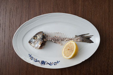 Fish bone left overs with a sliced lemon on a white oval plate.