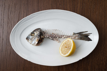 Fish bone left overs with a sliced lemon on a white oval plate.