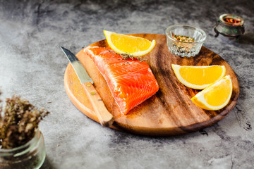 Fresh raw salmon steaks with pepper corns, salt, lemon and olive oil in an enamel bowl, on gray background. Healthy food, diet concept. Preparation for cooking fish with spices