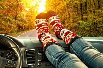 Woman legs with autumn socks in car interior and fall road background 