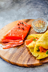 Thin pancakes with red fish on plate, top view.Crepes with filet salmon and cheese, red fish and green avocado on white plate over gray background.  Healthy breakfast