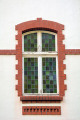 Fototapeta premium Beautiful stained glass green window decorated with orange brick. white wall.