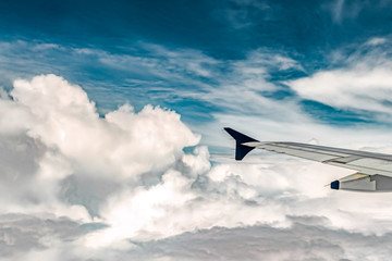 Fototapeta premium Mesmerizing natural view from Window side of an Airplane, cruising through White and Furry Cumulus Clouds with clear blue sky above it. Airplane wing parts flaps, pylon and winglet is visible - Image