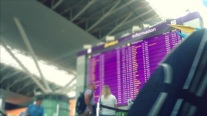 Defocusing. Departure board displaying flight information. Busy Airport Terminal. Traveler at airport. Side view of multiracial people standing in queue to check in in airport hall. 