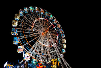 Giant Ferris Wheel with well illuminated cabins and decorated with colorful lights during night, is...