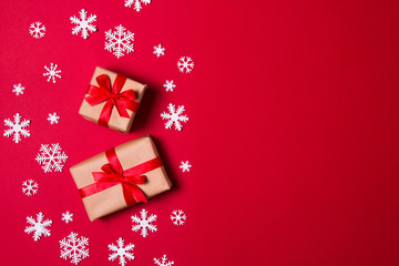 Christmas composition greeting card. Gift from craft paper on a red background with snowflakes. Top view, flat lay.