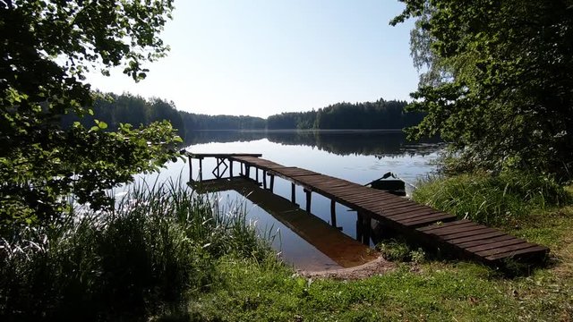 Wooden boat dock and calm lake water surface on sunny day. Slow motion