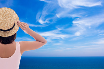 summer vacation and travel concept - back view of young woman in swimsuit and straw hat over blue sky background