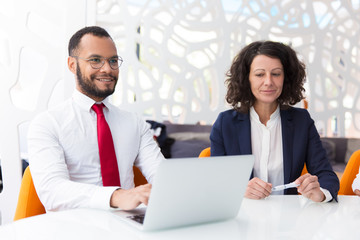 Excited business colleagues discussing deal with partners. Business man and woman sitting at meeting table with laptop and looking away. Business meeting concept