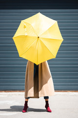 young adult woman in coat holding yellow umbrella outside