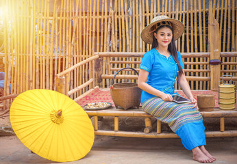 Asian women in blue local dresses using tablet or mobile device, Country life with yellow umbrella, tiffin carrier,Bamboo basket and Khene(Thai Musical Instruments), Technology in rural concept.
