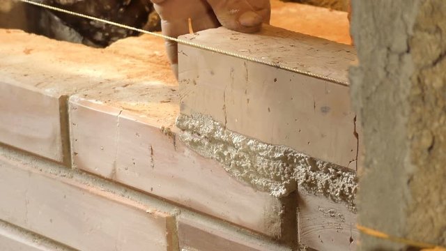 Mason bricklayer installing red brick with mortar for the chimney inside the house. Only hands visible. 