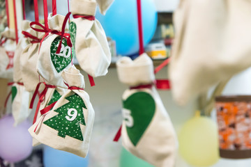 Self made Advent calendar linen bags sacks with Christmas tree ornament with dates tied with red silk ribbon hanging on string in kids room. Holiday preparations celebration