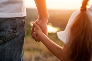Crop father and daughter holding hands in countryside