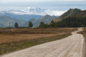 A dirt road leading to snowy peaks. Autumn landscape.