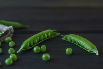 Pods of green peas and pea on a dark wooden surface. The concept of vegetarian food. Organic foods and fresh vegetables. Close up, top view, copy space