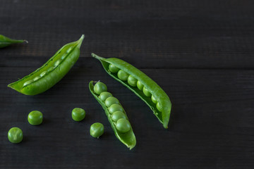 Pods of green peas and pea on a dark wooden surface. The concept of vegetarian food. Organic foods and fresh vegetables. Close up, top view, copy space