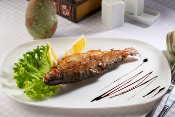 Roasted river fish on white plate, food close-up