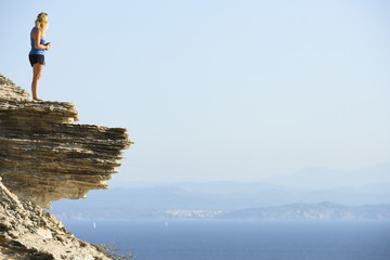 Obraz premium Stunning view of an unidentified blond girl on top of a limestone cliff overlooking the landscape during a beautiful sunset, Bonifacio, Corsica, France.
