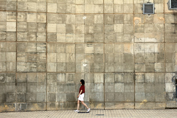 Una mujer andando con un muro tras ella