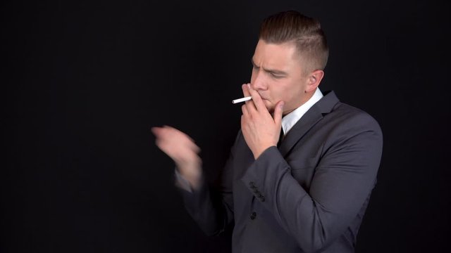 The young businessman could not light a cigarette and decided to quit smoking. Man in a black suit on a black background