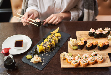 Four course lunch on special offer in luxury oriental restaurant. Elegant female client wrapped in blanket tasty delicious sushi set with seafood. Woman eating Japanese dish using food sticks.