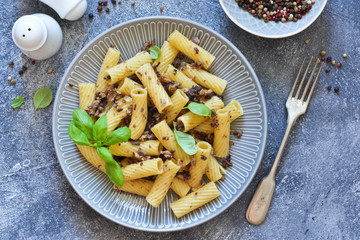 Rigatonni pasta with sauce and fried bacon on the kitchen table.