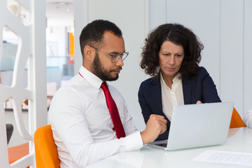 Obraz premium Business team of two using computer together. Business man and woman sitting at conference table with open laptop, looking at screen and reading. Teamwork concept