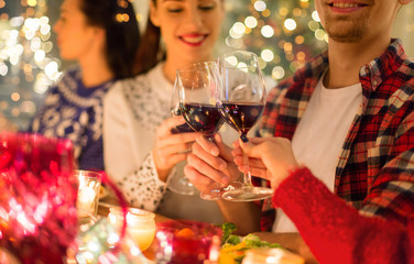 holidays and celebration concept - close up of happy friends having christmas dinner at home, drinking red wine and clinking glasses