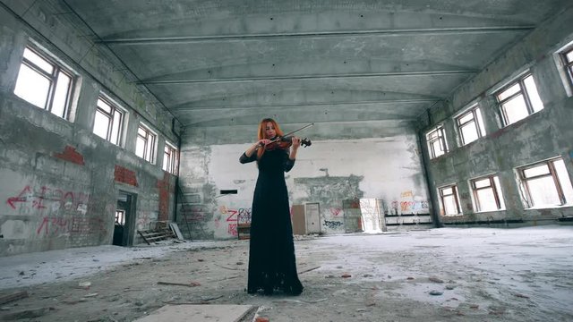 One fiddler playing wooden violin, standing in a room of ruined building.