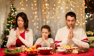 holidays, family and celebration concept - happy mother, father and little daughter having christmas dinner and praying before meal at home