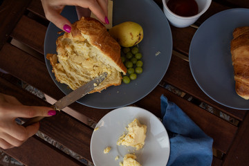 Flat view of breakfast in French style: female hands preparing croissant with butter 