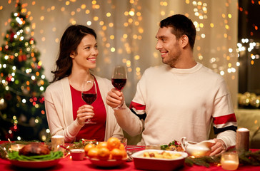 holidays, family and celebration concept - happy couple having christmas dinner at home and drinking red wine