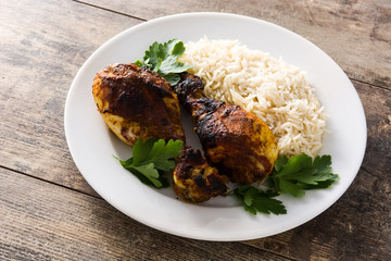 Roasted tandoori chicken with basmati rice in plate on wooden table.