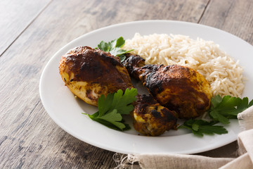 Roasted tandoori chicken with basmati rice in plate on wooden table.