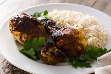 Roasted tandoori chicken with basmati rice in plate on wooden table.