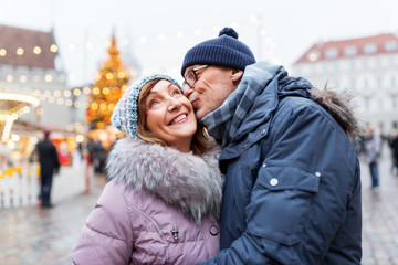 Fototapeta premium love, winter holidays and people concept - happy senior couple kissing at christmas market on town hall square in tallinn, estonia