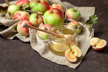 Ripe garden striped apples with leaves and a jar of honey on a beige napkin and textured background. Autumn harvest