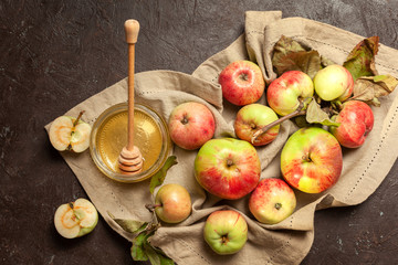 Ripe garden striped apples with leaves and a jar of honey on a beige napkin and textured background. Autumn harvest