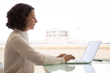 Focused female manager working on computer. Side of businesswoman sitting at workplace, using...