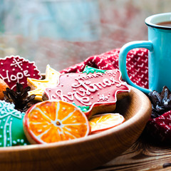 A cup of hot tea stands on a wooden table next to a wooden plate on which are gingerbread cookies made from orange slices against the background of a window with water drops