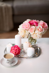 hygge and aromatherapy concept - burning candles, electric garland lights, cup of coffee and flowers on table