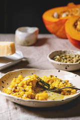 Eaten Traditional vegetarian pumpkin risotto italian dish in ceramic plate on linen table cloth with ingredients above. Dark rustic style
