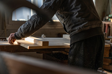 Cropped photo of old master carpenter in grey clothes that holding wooden boards in hand