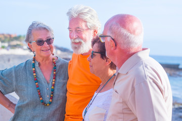 group of four happy seniors and mature people talking and having fun together at the beach with the sea at the background - friendship and relationship cocncept