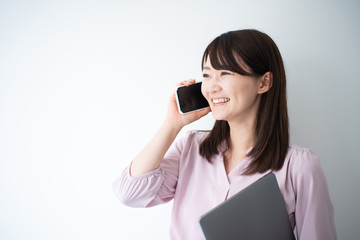 Fototapeta premium Young business woman holding smart phone and laptop computeragainst white wall