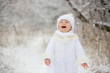 Cute little toddler boy and his older brothers, playing outdoors with snow on a winter day